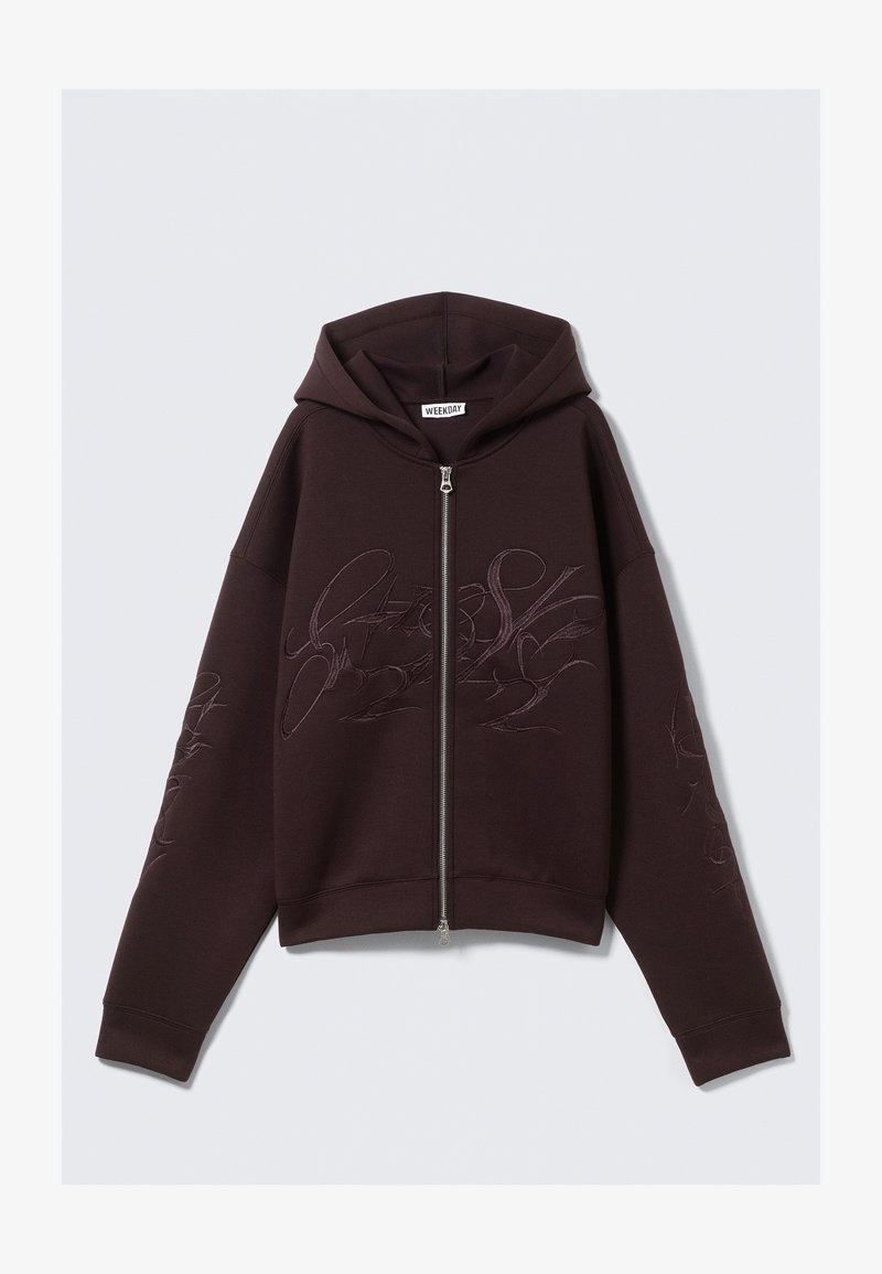 Haut à capuche zippé violet foncé avec une capuche ajustée, présentant des motifs brodés sur le devant et la manche, fabriqué en tissu doux et texturé.