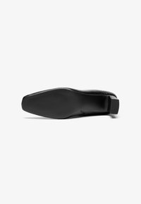 Pantof de piele neagră cu un design elegant, vârf pătrat, suprafață texturată și toc mic pătrat. Partea de jos are un grip cu model.