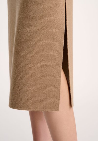 Knee-length beige skirt made from textured fabric featuring a side slit and clean hem, highlighting its simple design and neutral color.