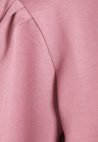 Gros plan sur un tissu rose avec une couture visible et un léger pli, montrant une texture lisse et douce ainsi qu'un motif de maille fine.