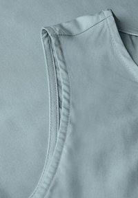 Light blue sleeveless shirt, made of smooth fabric, featuring flat edges and fine stitching along the neckline and armhole.
