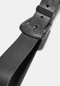 Čierny kožený opasok s textúrovanou prackou, ktorá má malé čierne cvoky, hladký vnútorný povrch a klasický rovný tvar.