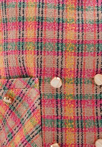 Multicolored tweed fabric featuring a check pattern in pink, green, and yellow, with prominent gold-toned buttons and a textured surface.