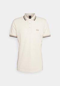 Pikétröja i off-white tyg, med en klassisk krage, treknappslinning och mörka randiga detaljer på kragen och ärmarna.