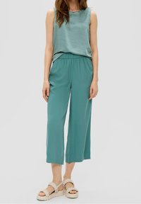 Licht teal mouwloos topje met een gestructureerde afwerking, gecombineerd met losse, cropped teal broeken en gevlochten neutrale sandalen.