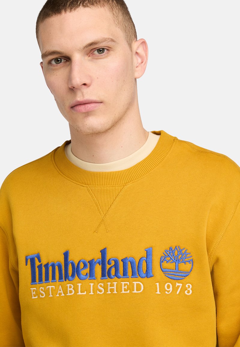 Felpa gialla in cotone, con logo blu ricamato e testo "Timberland ESTABLISHED 1973" sul davanti. Collo rotondo.