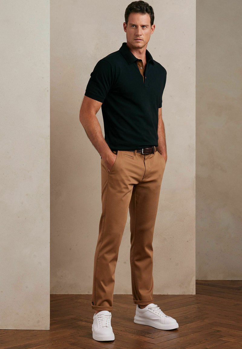 Czarna koszulka polo, beżowe spodnie i białe trampki. Koszulka ma kołnierzyk i guziki. Spodnie są dopasowane, z bocznymi kieszeniami, noszone z brązowym paskiem.