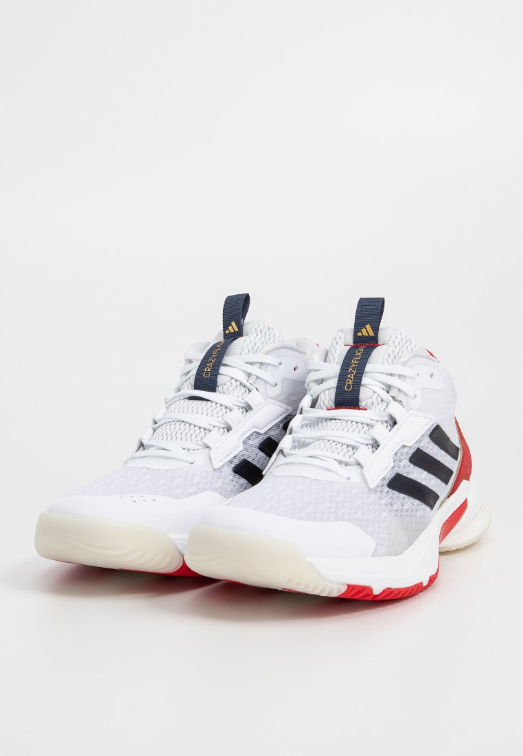 Zapatillas deportivas blancas con parte superior de malla, rayas negras y acentos rojos. Cuentan con una suela de goma y una pestaña de tiro azul marino en contraste.