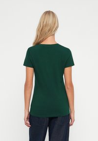 Zelené tričko s krátkým rukávem vyrobené z bavlny, má kulatý výstřih a přiléhavý střih, hladkou texturu a minimalistický styl.