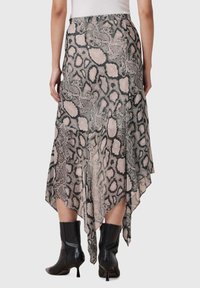 Asymmetrische rok in een slangenprint, gemaakt van een lichte, vloeiende stof in tinten beige en zwart, gecombineerd met puntige zwarte laarzen.