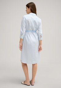 Vestito a righe blu chiaro con maniche tre quarti, vita con cintura e dettaglio a bottoni al colletto. Realizzato in tessuto liscio con spacchi laterali.