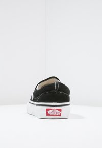 Baskets Vans noires vues de dos, semelle blanche avec logo rouge "Vans Off The Wall" sur le talon, couture blanche visible.