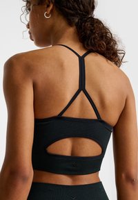 Zwarte sportbeha met een lage ruglijn, racerbackbandjes en een gestructureerde afwerking. Heeft een uitsnijding en versterkte naden.