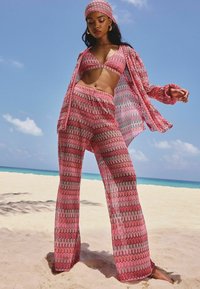Roze gemusterde zwemkledingset met een bralette top, uitlopende broek en een bijpassende hoofdband, ontworpen met golvende lijnen en van lichtgewicht stof.