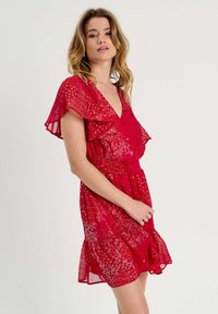 Vestido floral rojo con escote en V, mangas cortas con vuelo, cintura fruncida y falda en capas. Tejido ligero y semi-translúcido con un patrón texturizado.