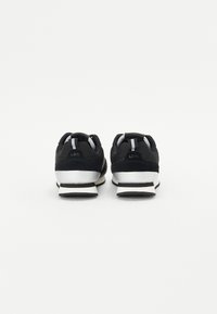 Sneaker nere in materiali scamosciato e mesh, con suola bianca, strisce nere e bianche, e una linguetta sul tallone.