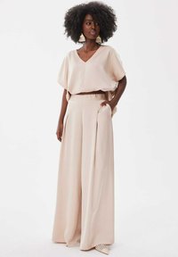 Beige cropped top met een V-hals en brede korte mouwen, gecombineerd met high-waisted, wijde broekspijpen met plooien en zijzakken.