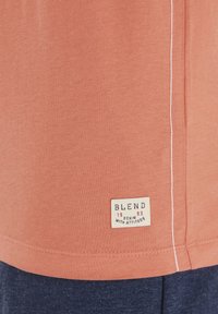 Rozsszínű, rövidujjú póló, fehér varrott varrással és négyzet alakú márkajelzővel, amelyen a "BLEND" felirat navy és piros színben szerepel. Puha pamut anyag.
