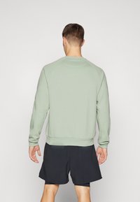 Felpa verde chiaro con maniche raglan, polsini e orlo a coste. Indossata con pantaloni corti neri, mostra una vestibilità rilassata e una texture morbida.