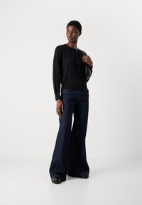 Svart langermet cardigan med rund hals og knappestolpe. Kombinert med mørkeblå vide jeans. Glatt tekstur, avslappet passform.