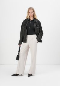 Zwarte denimbroek over een zwarte polo met knopen, crèmekleurige wijde broek, zwarte puntige ballerina's en een kleine zwarte handtas.