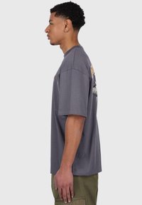 Gray cotton t-shirt with short sleeves, featuring a graphic design on the back and a relaxed fit. Visible stitching at the hem and cuffs.