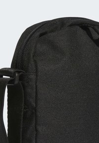 Bolsa de tela negra con superficie texturizada, cierre de cremallera y correa ajustable para llevar. Diseño compacto adecuado para diversos usos.
