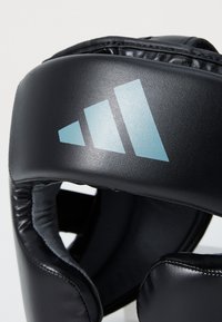 Coiffe en rembourrage noir avec une finition mate, arborant un logo triangulaire bleu clair. Intérieur doublé d'un matériau gris doux pour le confort.