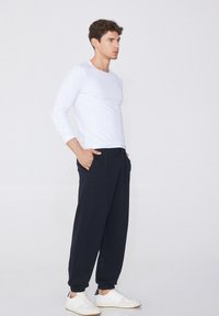 Camisa blanca de manga larga combinada con pantalones de chándal azul oscuro y zapatillas blancas. Los pantalones tienen bolsillos laterales y puños ajustados. Diseño simple y casual.