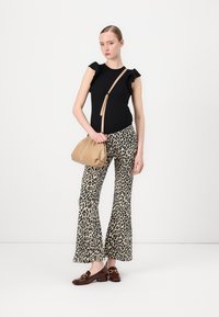 Top noir avec des manches volantées, pantalon évasé imprimé léopard et sac beige ; le mannequin porte des chaussures marron avec des accents dorés.