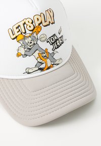 Hvitt cap med grå skygge, med animerte karakterer Tom og Jerry. Teksten sier "LA OSS SPILE." Skyggen har horisontal ribbet tekstur.