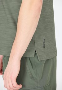Olivegrøn athletic skjorte med korte ærmer, tekstureret stof, sideskårede detaljer og "Dry Function" branding nær kanten, parret med matchende shorts.