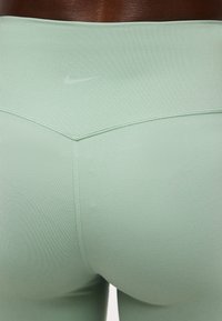 Κοντινό πλάνο ανοιχτοπράσινου εφαρμοστού αθλητικού κολάν με εμφανείς ραφές και διακριτικό λευκό λογότυπο Nike στη πίσω μέση.