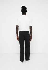 Czarne spodnie o prostym kroju, z kieszeniami i teksturowanym materiałem. Połączone z gładką białą koszulką z krótkim rękawem.