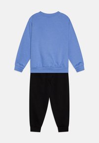 Sinine pusa, millel on soonikkoes varrukate ja hem, koos mustade trennipükstega, mõlemad pehmest kangast, nautides lahedat lõiget ja lihtsat disaini.