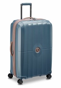 Valigia rigida, esterno blu con texture, zip in oro rosa, manico retrattile, quattro ruote nere, dettaglio del logo circolare sul fronte.