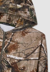 Felpa con zip mimetica in tonalità di marrone e verde, caratterizzata da un motivo ispirato alla natura con rami e pigne. Realizzata in tessuto morbido, include un cappuccio.