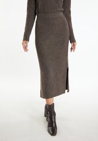 Gebreide bruine rok met geribbelde textuur, voorzien van een zijsplit en diamantmotief, gecombineerd met zwarte enkelboots.