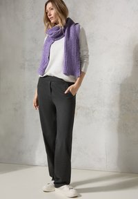 Écharpe violet côtelé, pull gris clair, pantalon foncé avec poches, baskets blanches. Textures douces et palette de couleurs neutres.