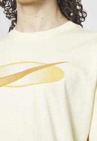 Camiseta de algodón amarillo claro con un gran diseño gráfico amarillento con patrones punteados. Cuello redondo y mangas cortas, textura suave.