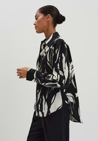 Camicia oversize in bianco e nero con audaci motivi a foglie, chiusura a bottoni sul davanti e maniche lunghe con dettagli ai polsini.
