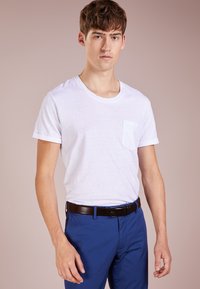 T-shirt blanc à manches courtes avec une poche sur la poitrine, porté avec un pantalon bleu et une ceinture noire. Design simple et classique, avec une texture douce.