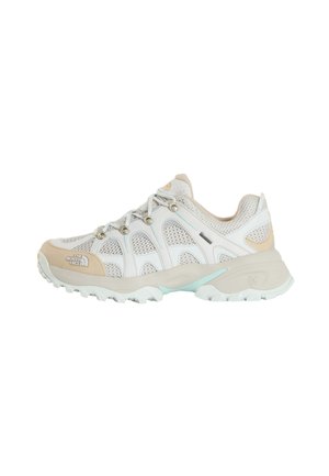 Zapato de senderismo blanco y beige con paneles de malla, ojales metálicos, suela de goma y logo de The North Face en la puntera y el lateral.