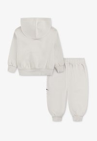 Ljusgrå hoodie med huva och elastiska muddar, kombinerad med matchande ljusgrå joggingbyxor med elastisk midja och sidodetalj.