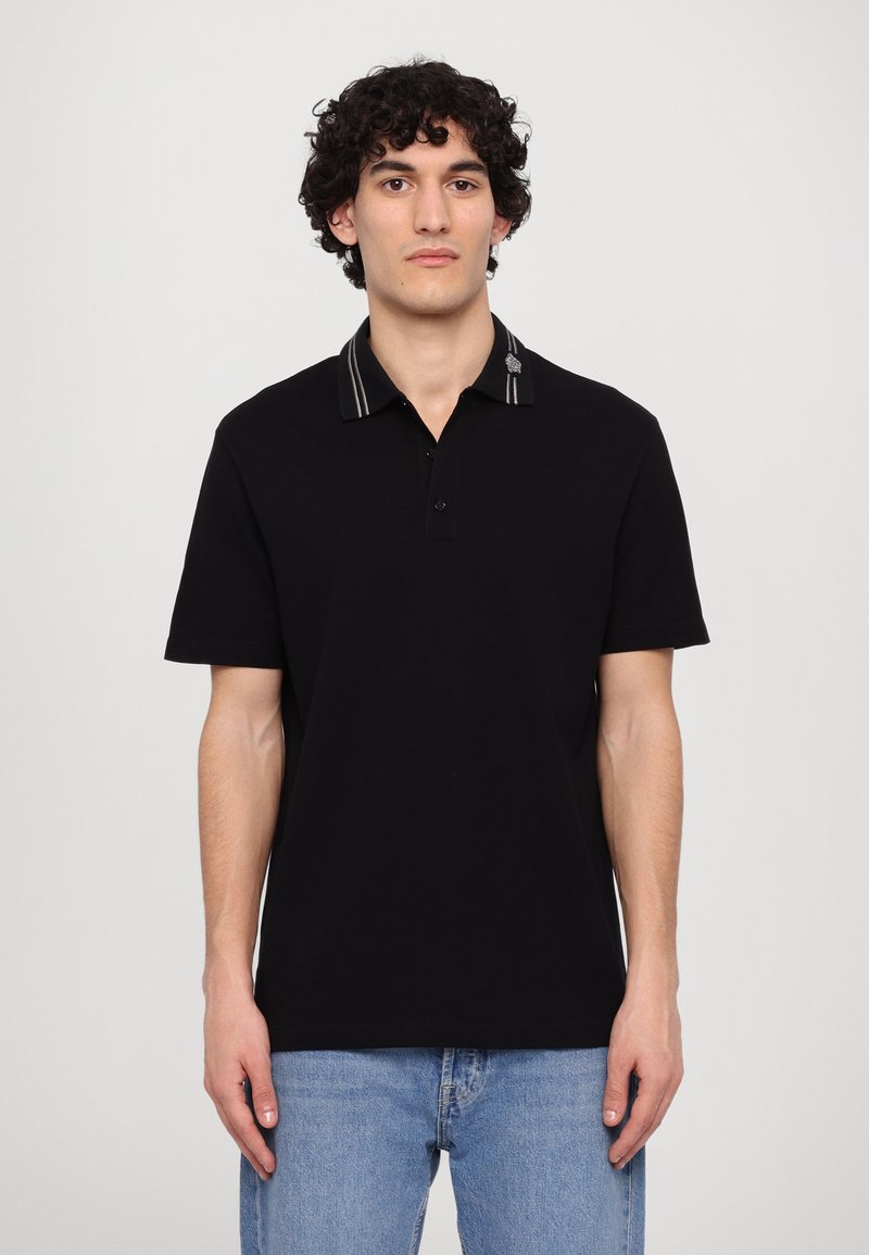 Svart polo t-shirt med krage som har randiga detaljer. Korta ärmar, en figurnära design och en enkel knäppning vid kragen.