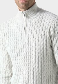 Maglione grigio chiaro con zip, caratterizzato da un motivo a diamond testurizzato, colletto alto a coste e una zip argentata.