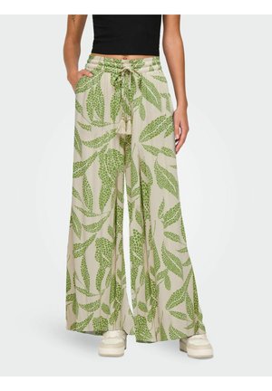 Beige vide bukser med grønt bladmønster, snor i midjen, brukt med svart croptopp og hvite joggesko.