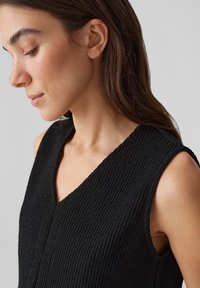 Schwarzes ärmelloses Top aus strukturiertem Strickstoff mit V-Ausschnitt, das eine leicht lockere Passform bietet und ein minimalistisches Design betont.