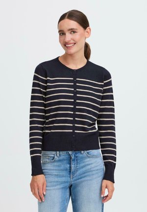 Marineblå cardigan med cremefarvede striber, rund halsudskæring, knaplukning foran og lange ærmer. Ribbet nederkant og manchetter, strikket struktur, båret med lyseblå jeans.