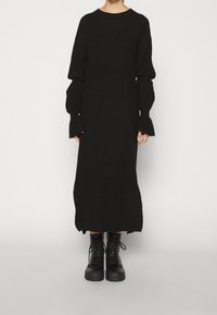 Svart stickad klänning med långa ärmar, lös passform, ribbad textur och sidslitsar. Kombinerad med svarta snörstövlar av combat-typ.